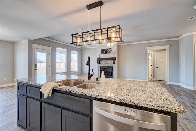 kitchen with stainless steel dishwasher, a kitchen island with sink, crown molding, sink, and a fireplace