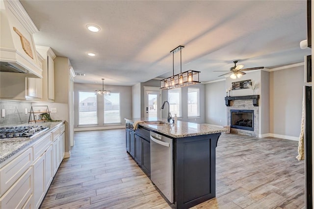 kitchen with sink, hanging light fixtures, a fireplace, an island with sink, and stainless steel appliances