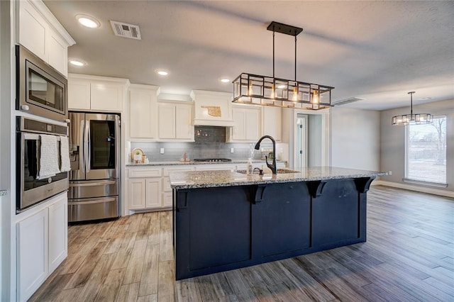 kitchen with a center island with sink, light stone countertops, white cabinetry, and stainless steel appliances