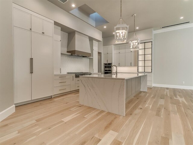 kitchen featuring a spacious island, wall chimney exhaust hood, light wood-type flooring, appliances with stainless steel finishes, and white cabinetry