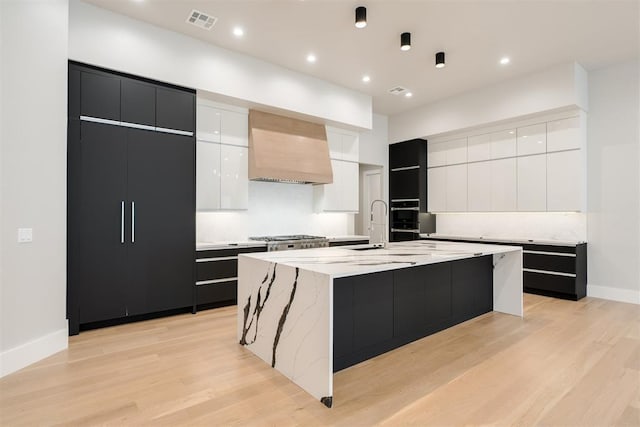 kitchen featuring white cabinets, custom range hood, light hardwood / wood-style flooring, and a spacious island