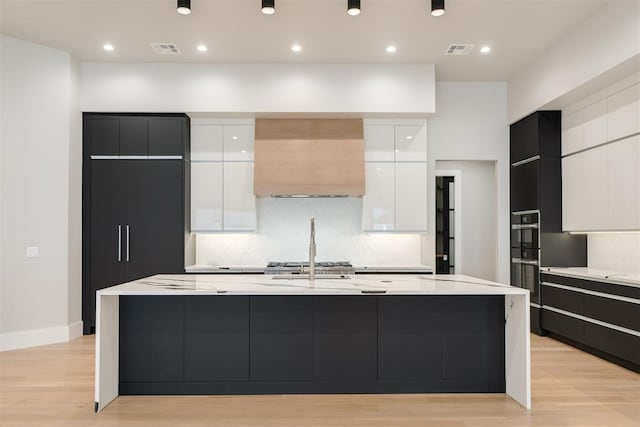 kitchen featuring light wood-type flooring, premium range hood, white cabinetry, and a spacious island