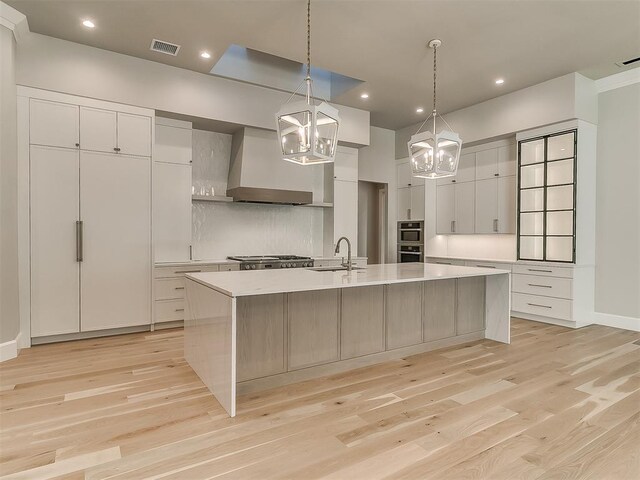 kitchen with premium range hood, decorative light fixtures, light hardwood / wood-style flooring, a large island, and white cabinetry