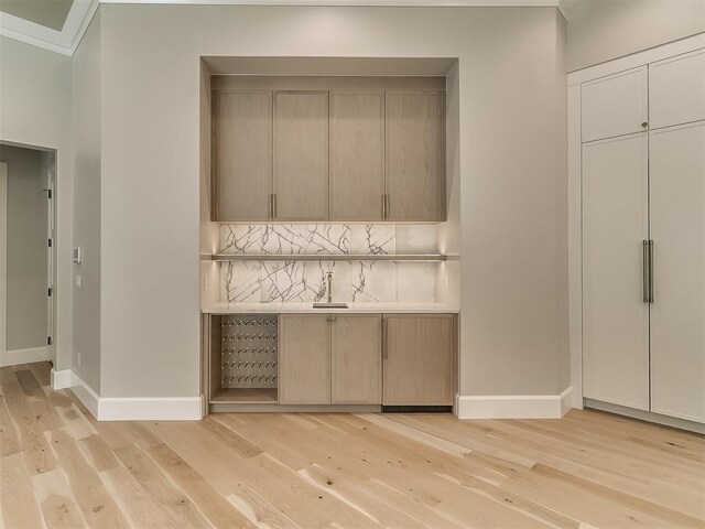 bar with tasteful backsplash, crown molding, sink, and light hardwood / wood-style floors