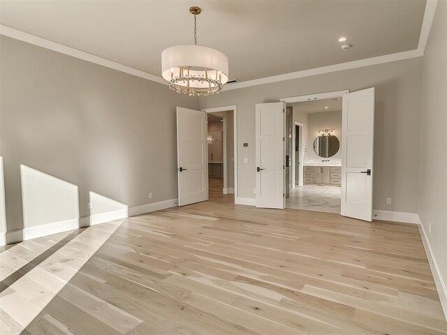 empty room featuring a notable chandelier, crown molding, and light hardwood / wood-style flooring