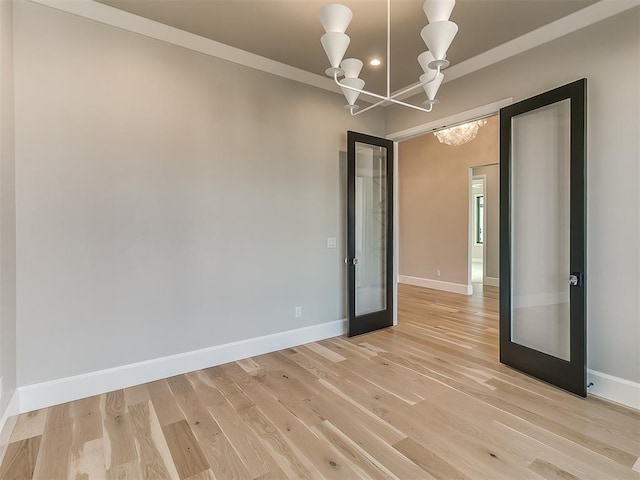 spare room featuring a chandelier, french doors, light wood-type flooring, and ornamental molding