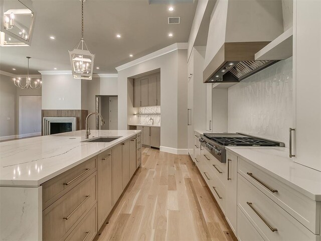 kitchen with a large island with sink, wall chimney exhaust hood, tasteful backsplash, decorative light fixtures, and stainless steel gas cooktop