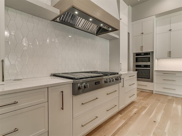 kitchen with appliances with stainless steel finishes, tasteful backsplash, light stone counters, white cabinetry, and extractor fan