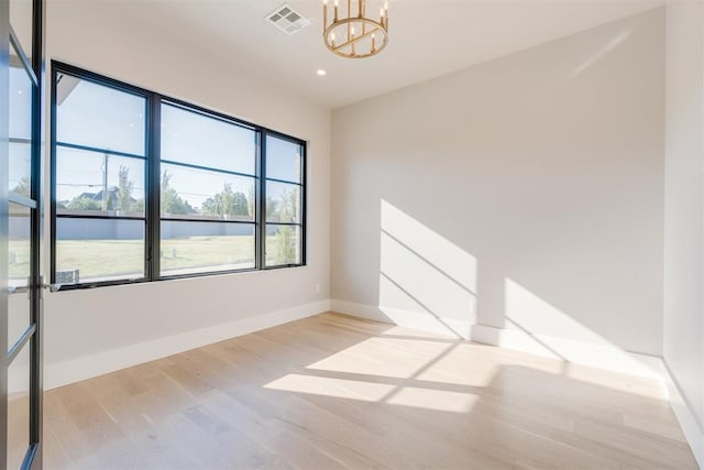 spare room with light wood-type flooring and an inviting chandelier