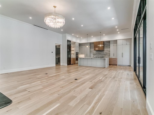 unfurnished living room with light wood-type flooring, crown molding, and a notable chandelier