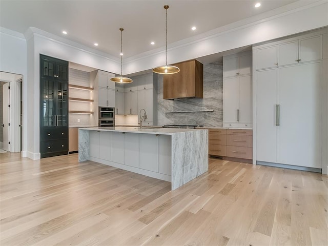 kitchen featuring gray cabinetry, a large island, light stone countertops, hanging light fixtures, and backsplash