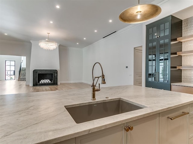 kitchen featuring sink, light stone countertops, hanging light fixtures, and ornamental molding