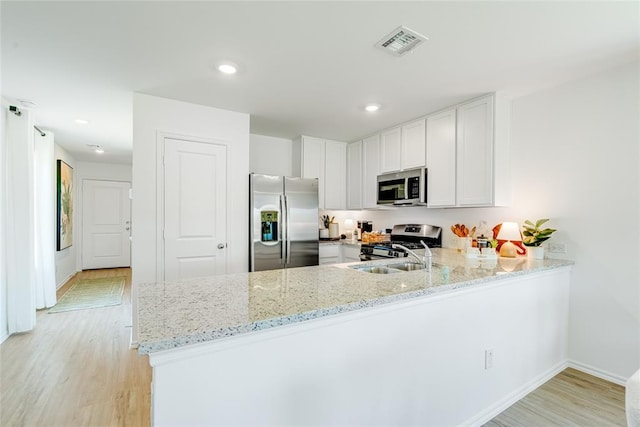 kitchen featuring kitchen peninsula, stainless steel appliances, white cabinetry, and light stone countertops