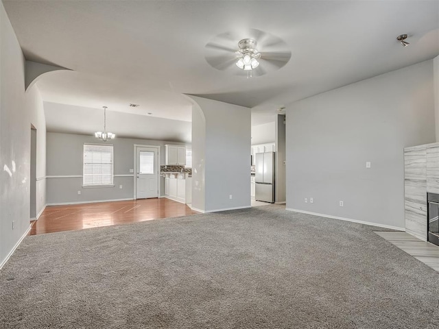 unfurnished living room featuring ceiling fan with notable chandelier, light colored carpet, and a fireplace