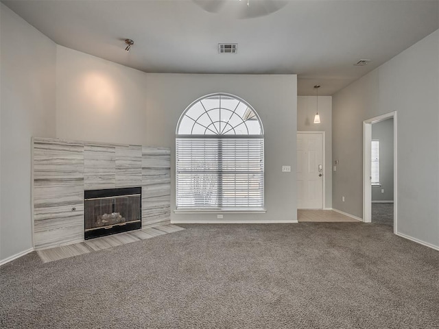 unfurnished living room with a tile fireplace, light colored carpet, and ceiling fan