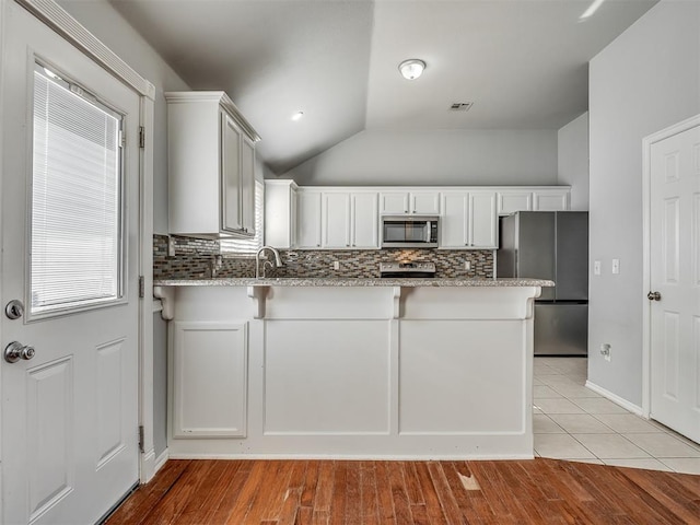 kitchen with white cabinetry, light stone counters, backsplash, vaulted ceiling, and appliances with stainless steel finishes