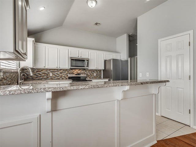 kitchen featuring white cabinets, appliances with stainless steel finishes, light stone counters, and lofted ceiling