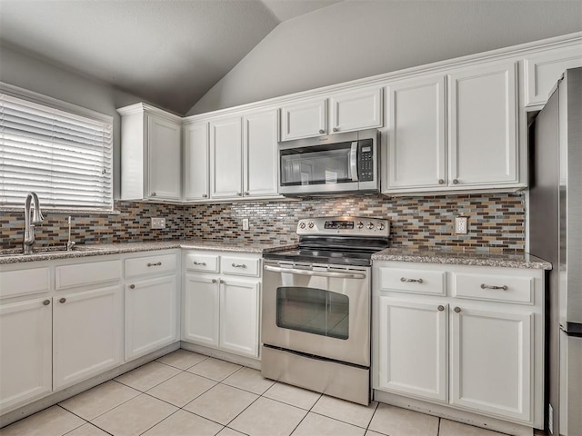 kitchen featuring sink, white cabinets, lofted ceiling, light tile patterned floors, and appliances with stainless steel finishes