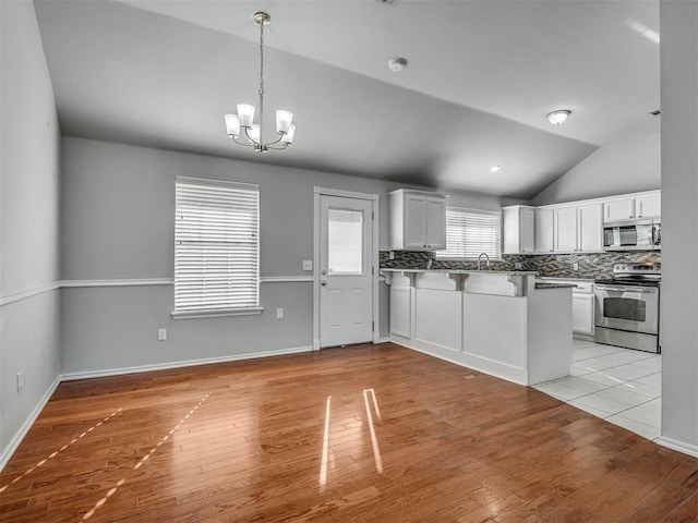 kitchen with lofted ceiling, white cabinets, tasteful backsplash, light hardwood / wood-style floors, and stainless steel appliances