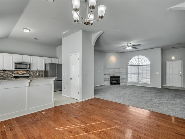 kitchen featuring decorative backsplash, ceiling fan with notable chandelier, stainless steel appliances, a tile fireplace, and white cabinetry