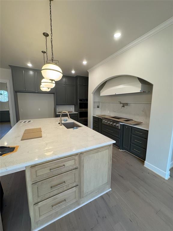 kitchen with light stone counters, sink, decorative light fixtures, and a kitchen island with sink