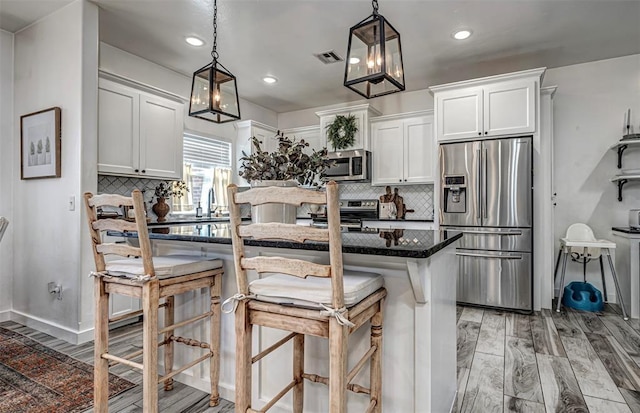 kitchen with a kitchen bar, white cabinets, pendant lighting, and appliances with stainless steel finishes