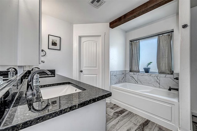 bathroom featuring beam ceiling, vanity, and a tub