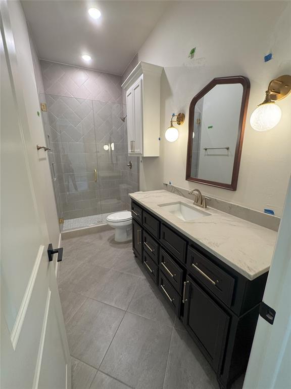 bathroom with a shower with door, vanity, tile patterned floors, and toilet