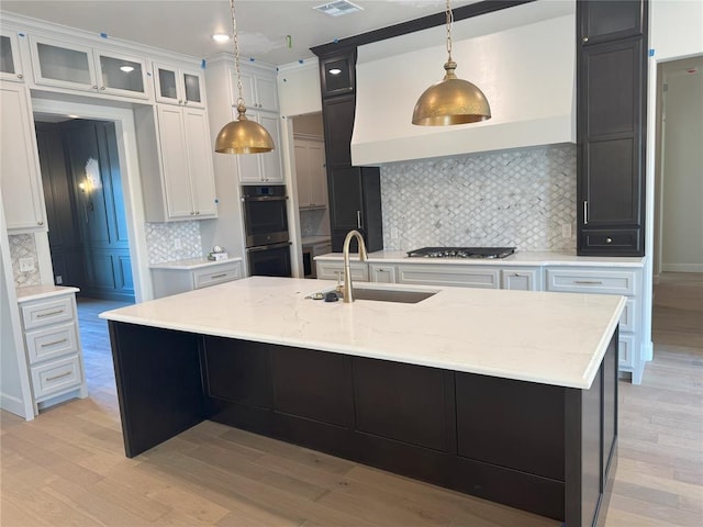 kitchen featuring stainless steel appliances, white cabinetry, a kitchen island with sink, and decorative backsplash