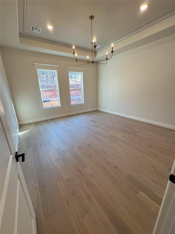 spare room featuring ornamental molding, light hardwood / wood-style flooring, an inviting chandelier, and a tray ceiling