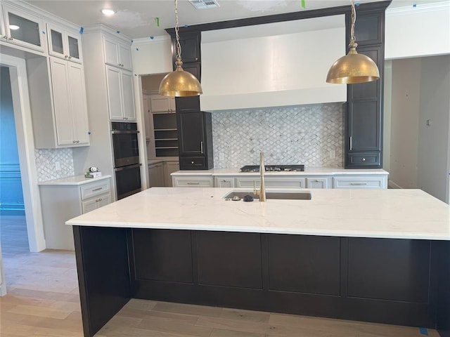 kitchen with light wood-type flooring, stainless steel double oven, a sink, and light stone countertops