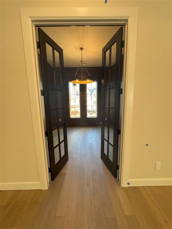 corridor featuring light wood-style floors, baseboards, and french doors