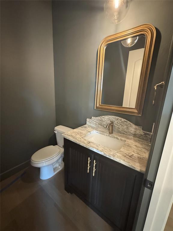 half bathroom with baseboards, vanity, and toilet