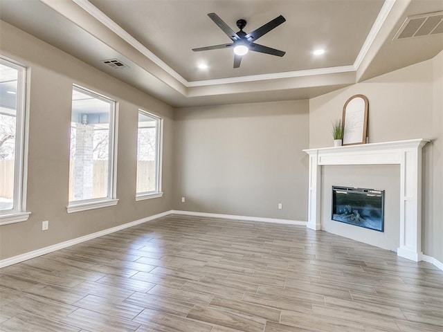 unfurnished living room with ceiling fan, a raised ceiling, and ornamental molding