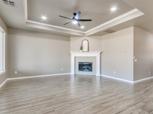 unfurnished living room featuring a raised ceiling, ceiling fan, and crown molding