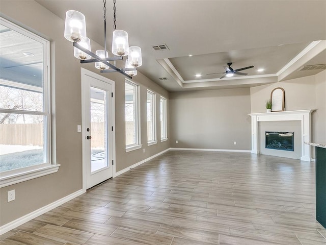 unfurnished living room featuring a raised ceiling, a wealth of natural light, and ceiling fan with notable chandelier