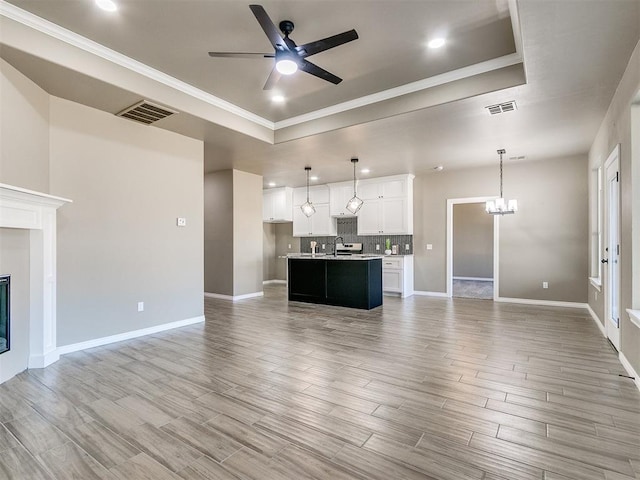 unfurnished living room with a tray ceiling, crown molding, sink, and ceiling fan with notable chandelier