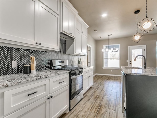 kitchen with pendant lighting, sink, stainless steel gas stove, light stone countertops, and white cabinetry