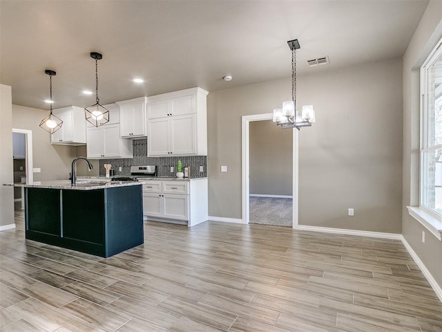 kitchen featuring light stone countertops, decorative light fixtures, white cabinetry, and sink