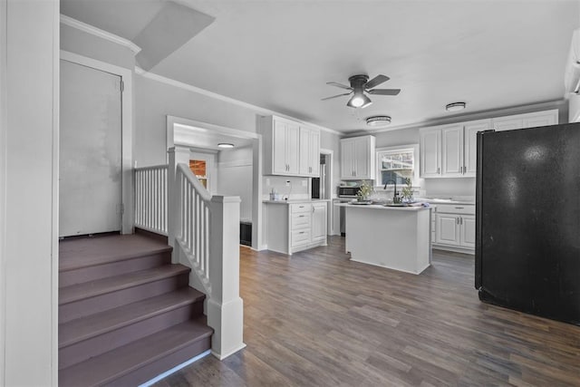 kitchen with ceiling fan, a kitchen island, crown molding, black refrigerator, and white cabinets