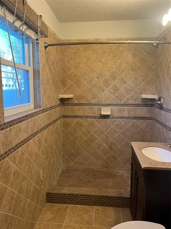 bathroom with tiled shower, tile patterned floors, toilet, a textured ceiling, and vanity