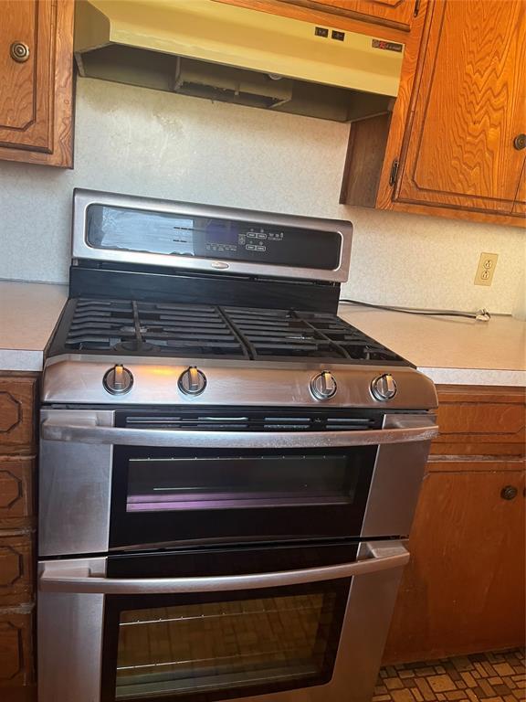 interior details featuring brown cabinets, light countertops, double oven range, and under cabinet range hood