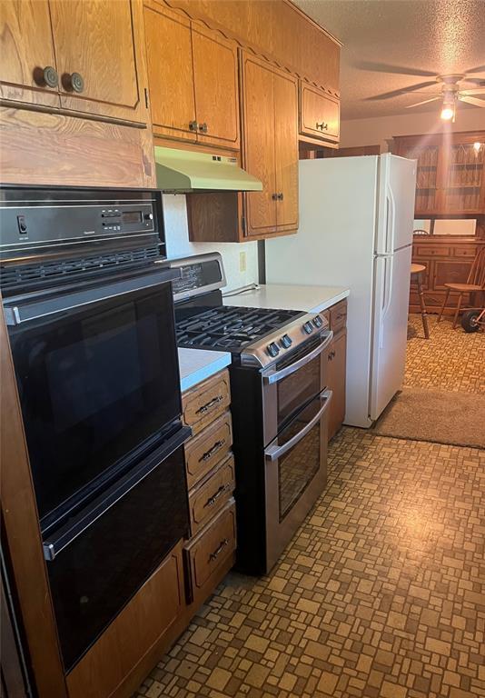 kitchen featuring oven, ceiling fan, range with two ovens, light countertops, and under cabinet range hood