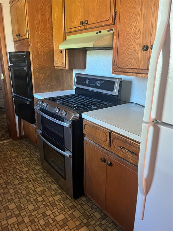 kitchen featuring oven, under cabinet range hood, light countertops, freestanding refrigerator, and double oven range