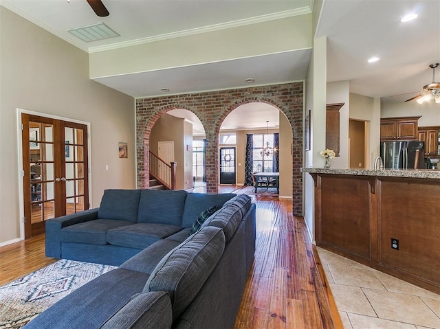 living room with ceiling fan with notable chandelier, french doors, light wood-type flooring, and brick wall