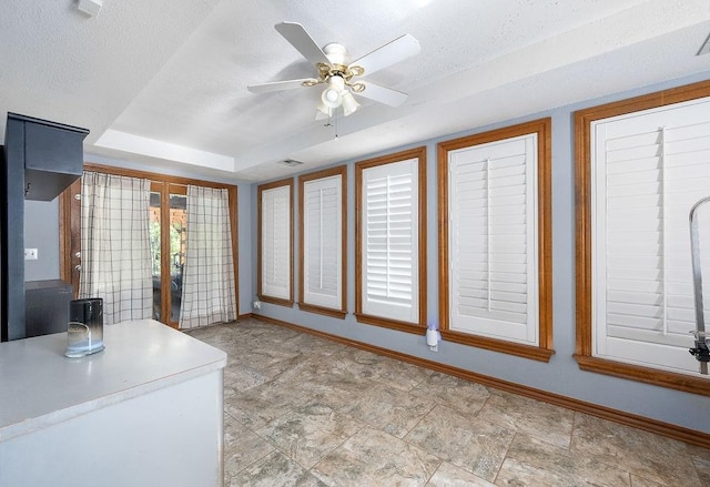 kitchen featuring ceiling fan, a raised ceiling, and a textured ceiling