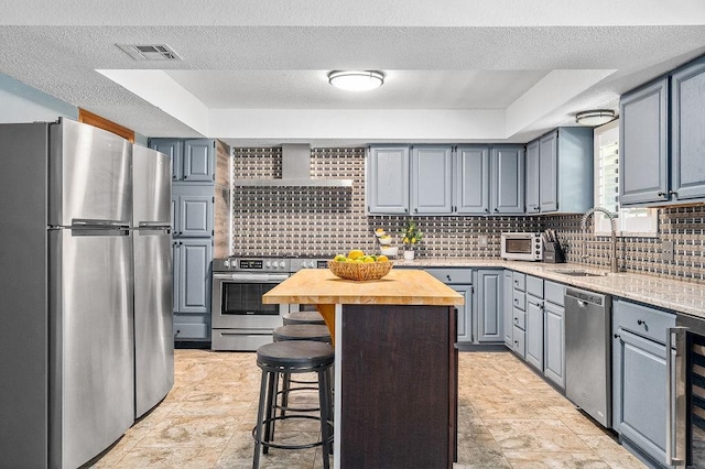 kitchen with a kitchen bar, appliances with stainless steel finishes, a raised ceiling, sink, and butcher block countertops