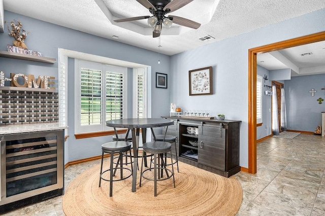 bar featuring a textured ceiling, a tray ceiling, wine cooler, and ceiling fan