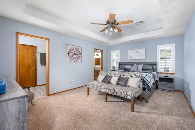 carpeted bedroom featuring a textured ceiling, a tray ceiling, ceiling fan, and ensuite bathroom