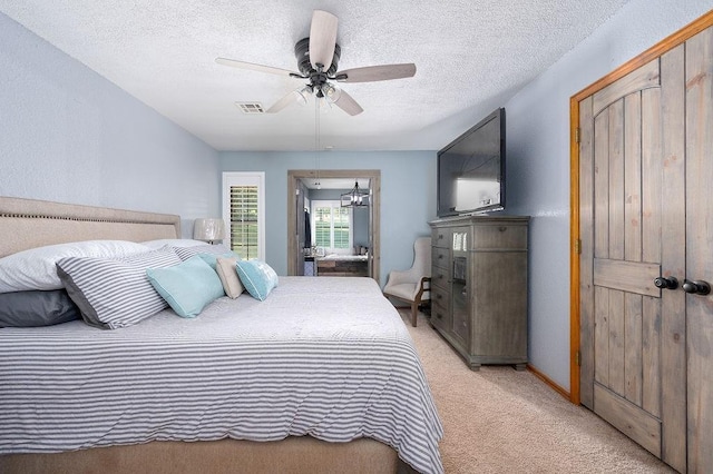 bedroom with ceiling fan, light carpet, and a textured ceiling